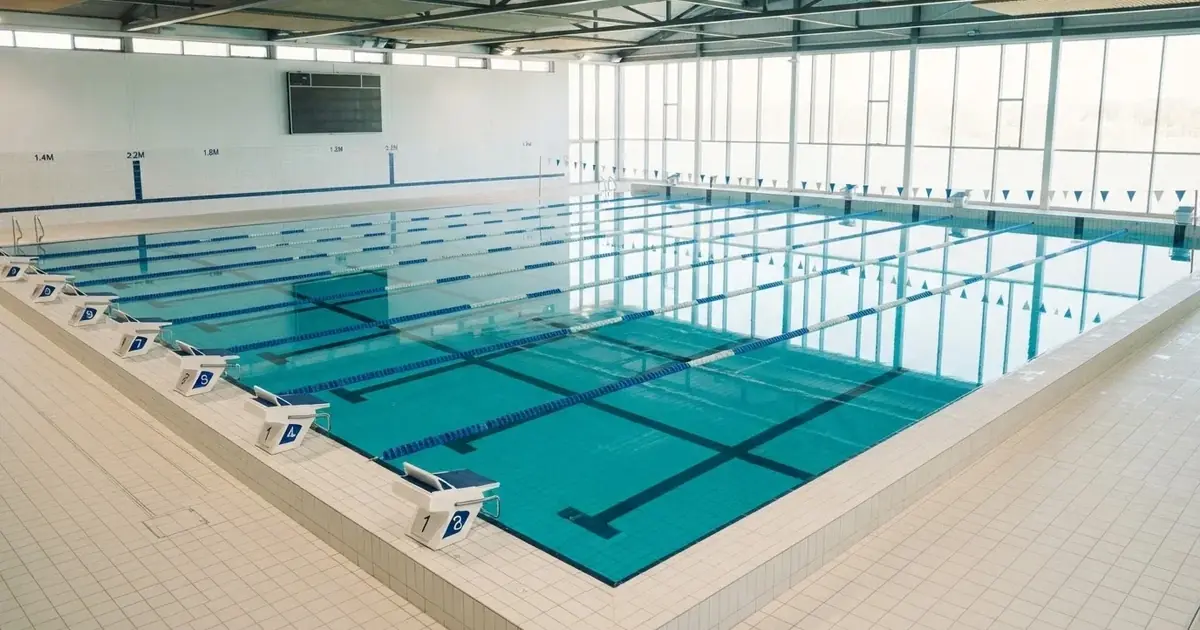 Pusty basen olimpijski z równymi torami i spokojną taflą wody, widok z trybun w jasnym świetle.