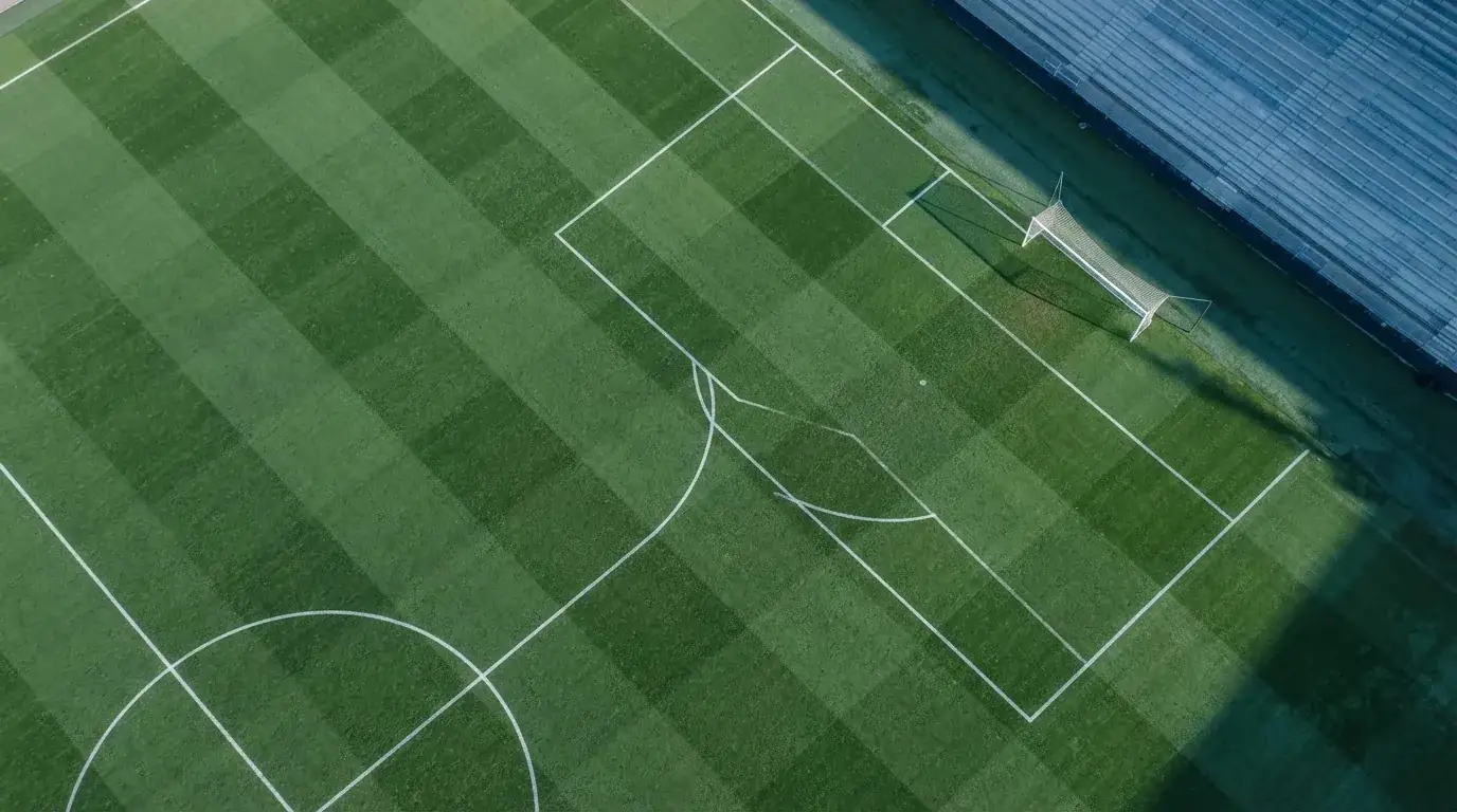 Murawa stadionu z wyraźnymi liniami pola karnego widziana z góry, bez ludzi, w świetle wczesnego poranka.